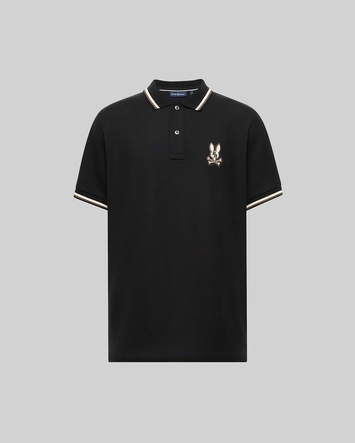 The Psycho Bunny MENS WADE PIQUE POLO (MT0100044) is a black Pima cotton polo for men, featuring white and beige colorblock trim on the collar and sleeves, plus an embroidered eagle crest logo on the left chest. Displayed on a plain gray background.