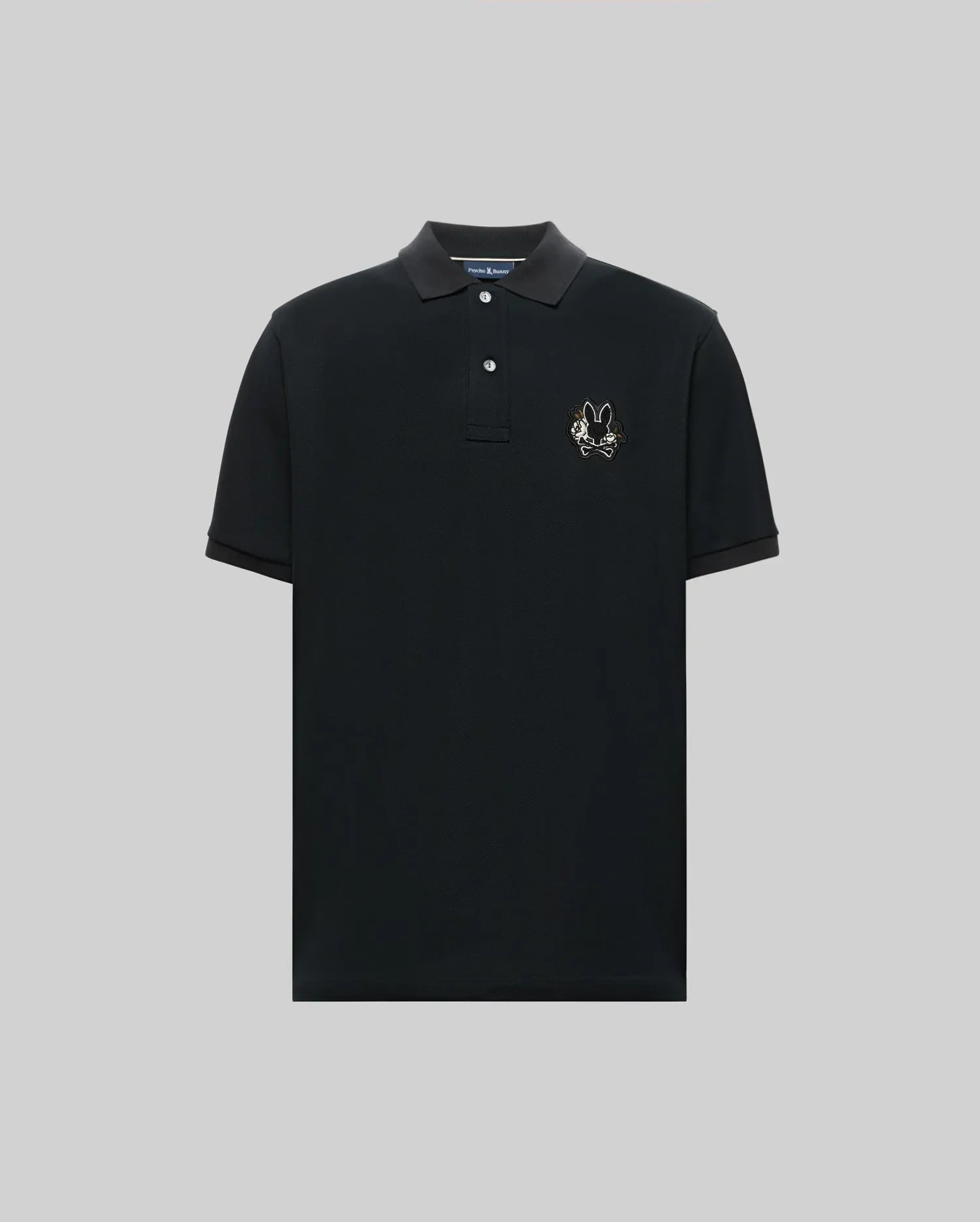 The Psycho Bunny MENS AUGUSTE PIQUE POLO SHIRT (MT0100051) is a black, short-sleeved collared polo with three buttons and an embroidered chenille bunny patch on the left chest, shown against a plain gray background. (5)
