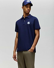 A person wears the Psycho Bunny MENS AUGUSTE PIQUE POLO SHIRT (MT0100051) in navy blue with a white embroidered logo, paired with khaki pants and a matching navy cap featuring the same white logo, against a plain light background. (1)