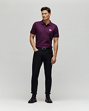 A man stands in a studio wearing the Psycho Bunny MENS AUGUSTE PIQUE POLO SHIRT - MT0100051 in dark purple, paired with black pants and boots. He smiles, looking to the side with one hand in his pocket against a plain light gray background.