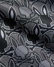 Mens Reeves All Over Bunny Sport Polo in black, white, and grey, featuring an all-over Psycho Bunny skull and crossbones print on a geometric striped performance fabric.