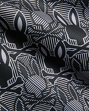 Mens Reeves All Over Bunny Sport Polo in black, white, and grey, featuring an all-over Psycho Bunny skull and crossbones print on a geometric striped performance fabric.
