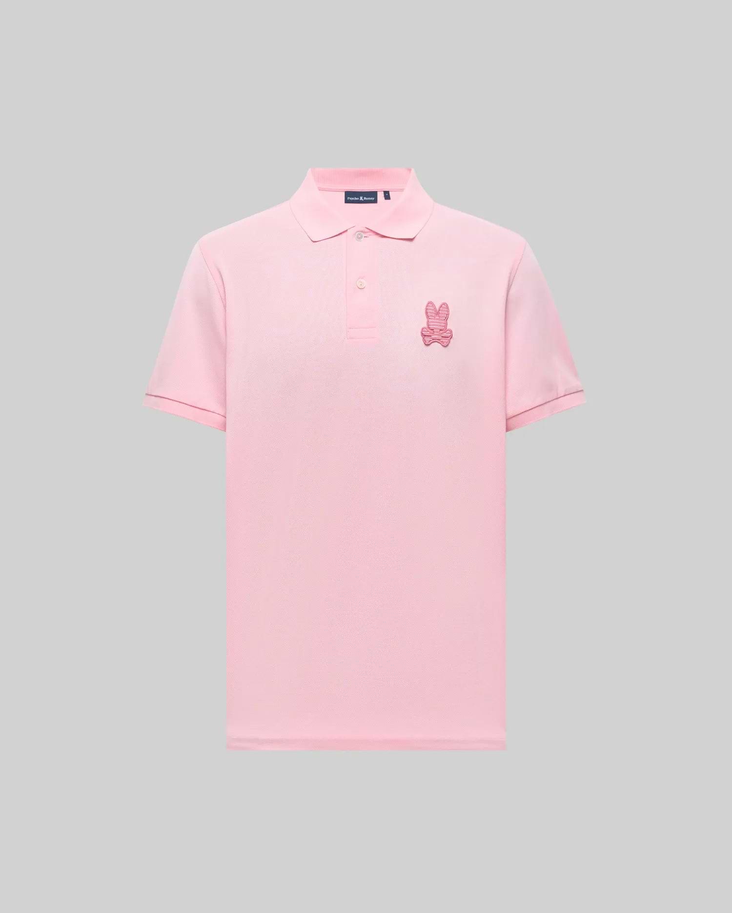 The Psycho Bunny MENS PATRICK POLO (MT0100095) is a light pink, 100% cotton knit short-sleeve shirt with a collar, button placket, and an embroidered pink bunny logo on the left chest, shown against a gray background. (4)