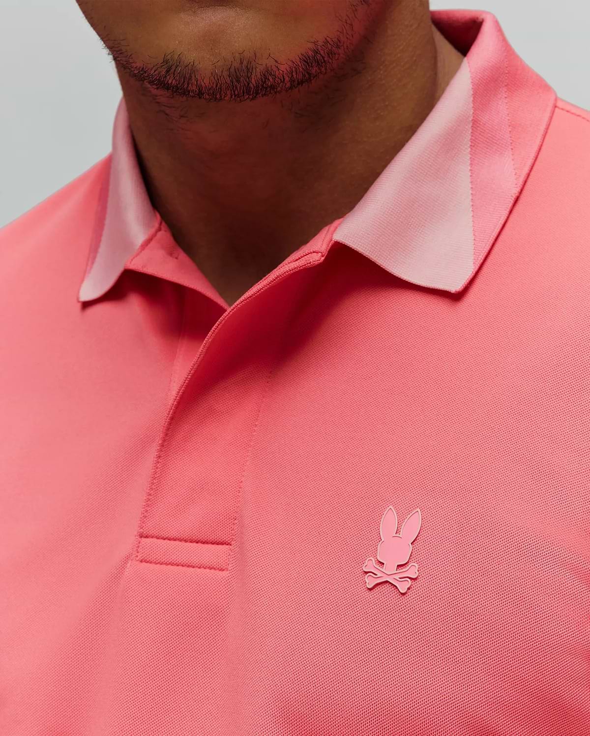 Mens Onyx Sport Polo in vibrant coral pique knit, featuring a lighter pink accent collar and a tonal embroidered Psycho Bunny skull logo on the left chest. (2)