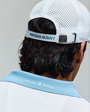 Mens Onyx Sport Polo in white pique with a light blue ribbed collar featuring white embroidered Psycho Bunny text and skull logo on the back, paired with a white perforated sport cap with light blue Psycho Bunny text and a metal bunny skull buckle. (3)
