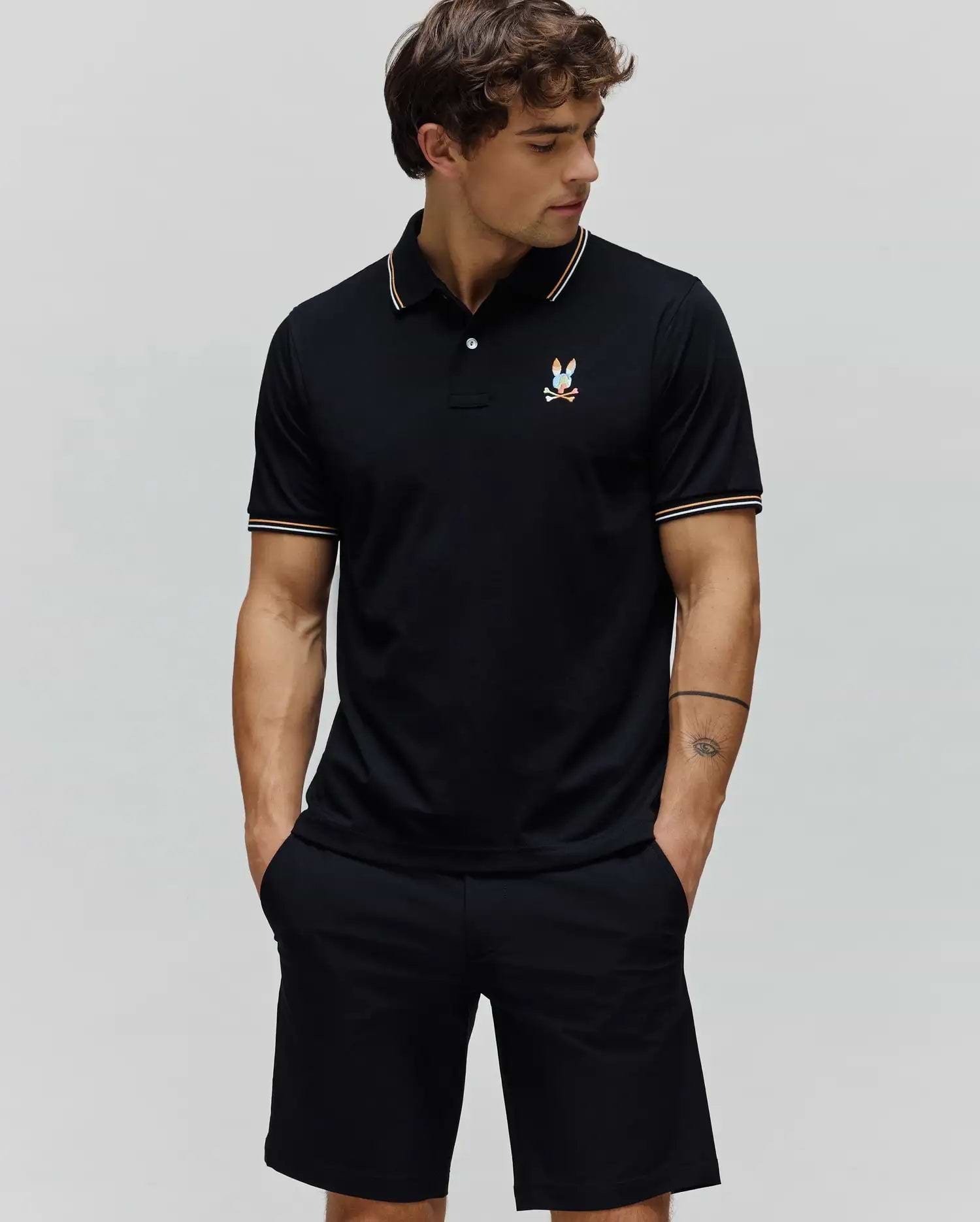 Black Mens Ara Pique Polo with a classic fit, featuring white and orange striped collar and cuffs, and a small, multi-color embroidered Psycho Bunny skull logo on the left chest.