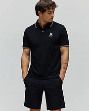 Black Mens Ara Pique Polo with a classic fit, featuring white and orange striped collar and cuffs, and a small, multi-color embroidered Psycho Bunny skull logo on the left chest.
