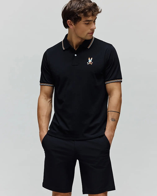 Black Mens Ara Pique Polo with a classic fit, featuring white and orange striped collar and cuffs, and a small, multi-color embroidered Psycho Bunny skull logo on the left chest.