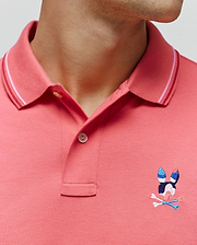 Mens Ara Pique Polo in coral pink, featuring a classic fit, pique knit texture, ribbed collar with white and dark pink stripes, and a small, embroidered multi-color Psycho Bunny skull logo on the left chest. (2)