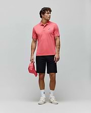Mens Ara Pique Polo in coral, classic fit, with white tipping and a multi-color embroidered bunny skull logo on the left chest. Black shorts, white bunny skull socks, and beige sneakers. (4)