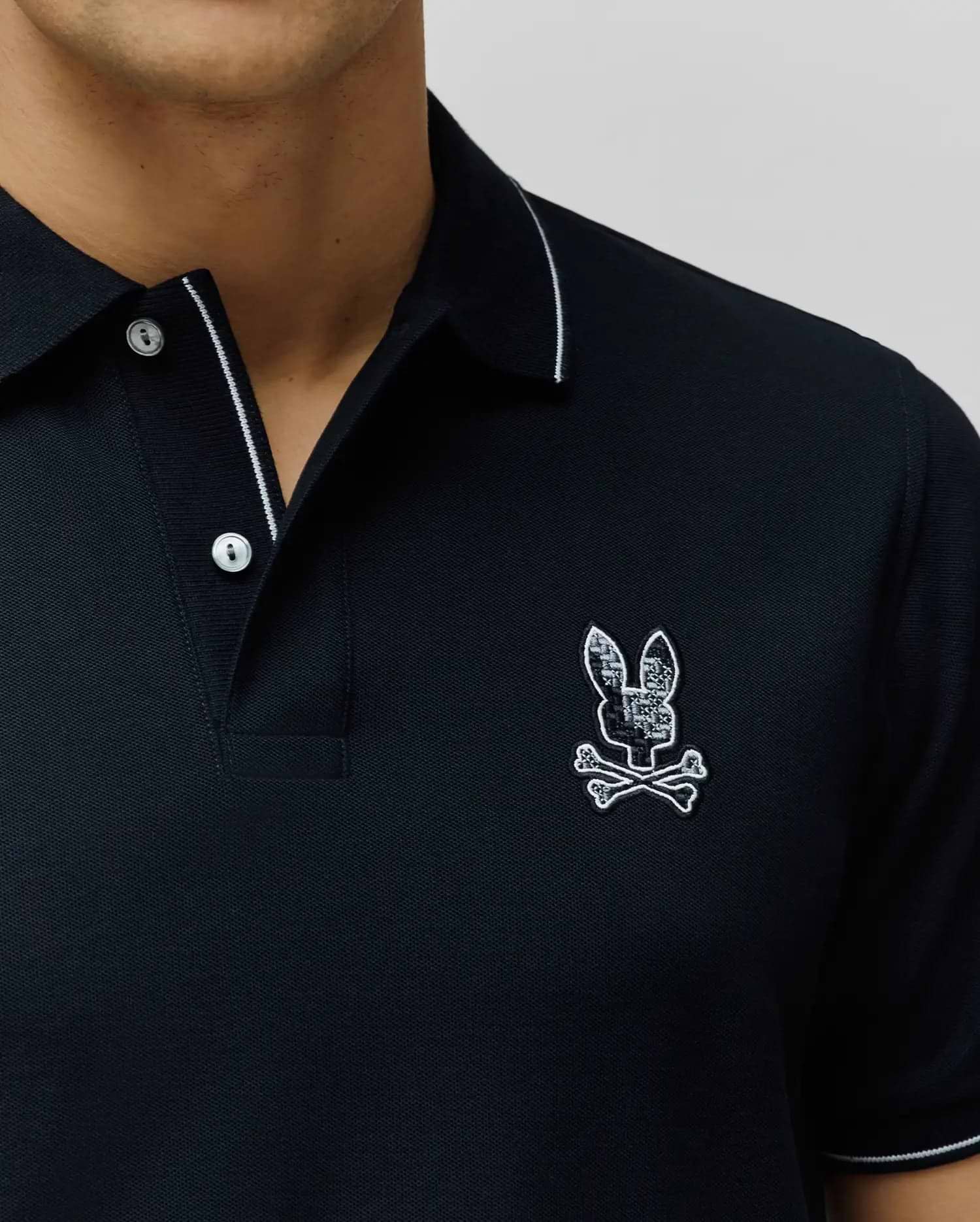Black Mens Olivier Pique Polo, classic fit, with white tipping on collar and sleeves, two white buttons, and a detailed embroidered black and white patterned Psycho Bunny skull logo on the left chest. (2)