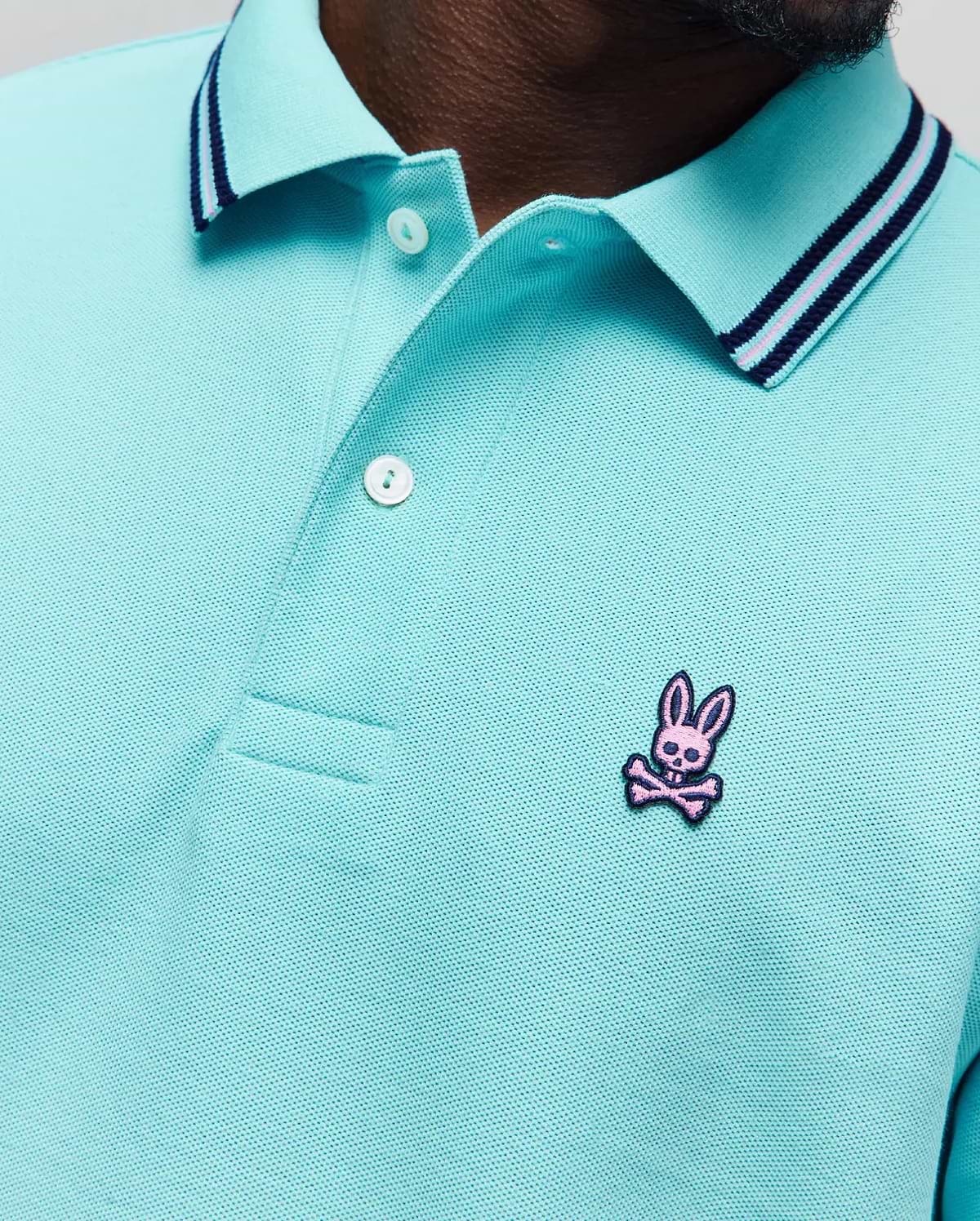 Mens Clark Pique Polo in aqua, featuring a classic fit, textured pique fabric, a ribbed collar with navy and pink stripes, and a small embroidered pink Psycho Bunny skull logo on the left chest. (2)