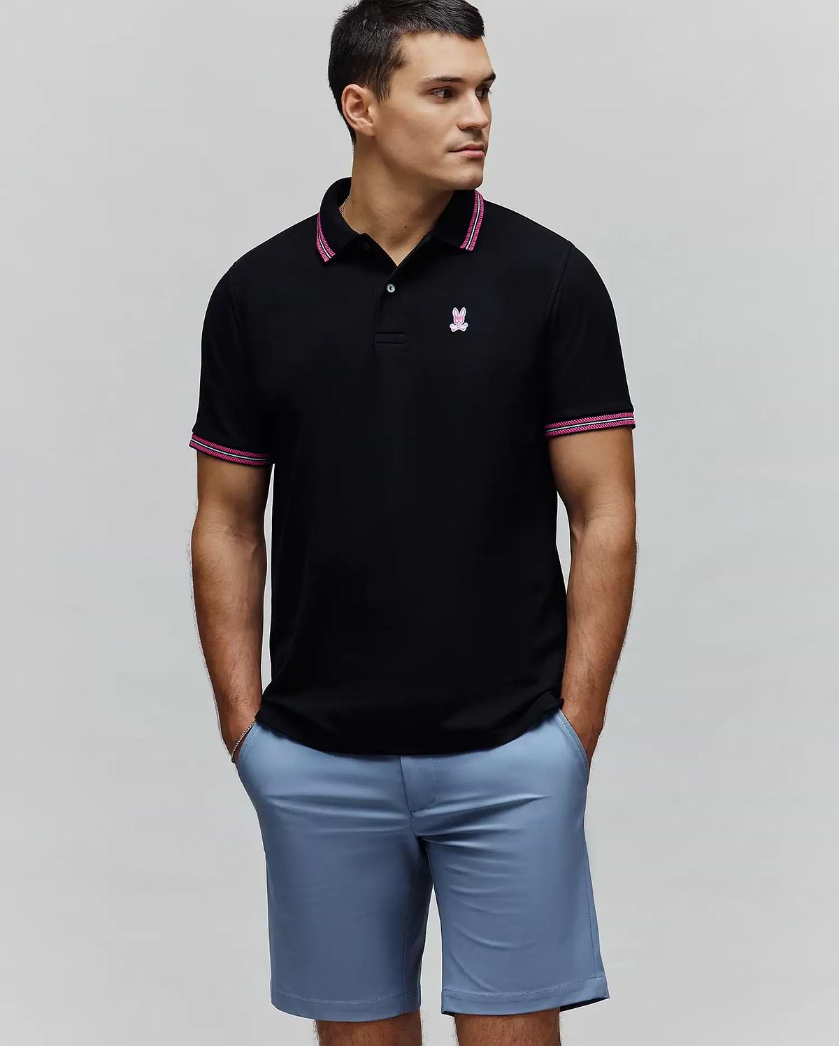 Mens Clark Pique Polo. Black classic fit pique polo with a small embroidered pink Psycho Bunny skull logo on the left chest, accented by pink and white striped collar and sleeve cuffs.