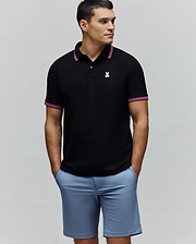 Mens Clark Pique Polo. Black classic fit pique polo with a small embroidered pink Psycho Bunny skull logo on the left chest, accented by pink and white striped collar and sleeve cuffs.