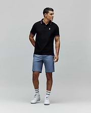 Black Mens Clark Pique Polo with classic fit, pique texture, featuring a small embroidered pink Psycho Bunny skull logo on the left chest, and pink striped collar and cuffs.