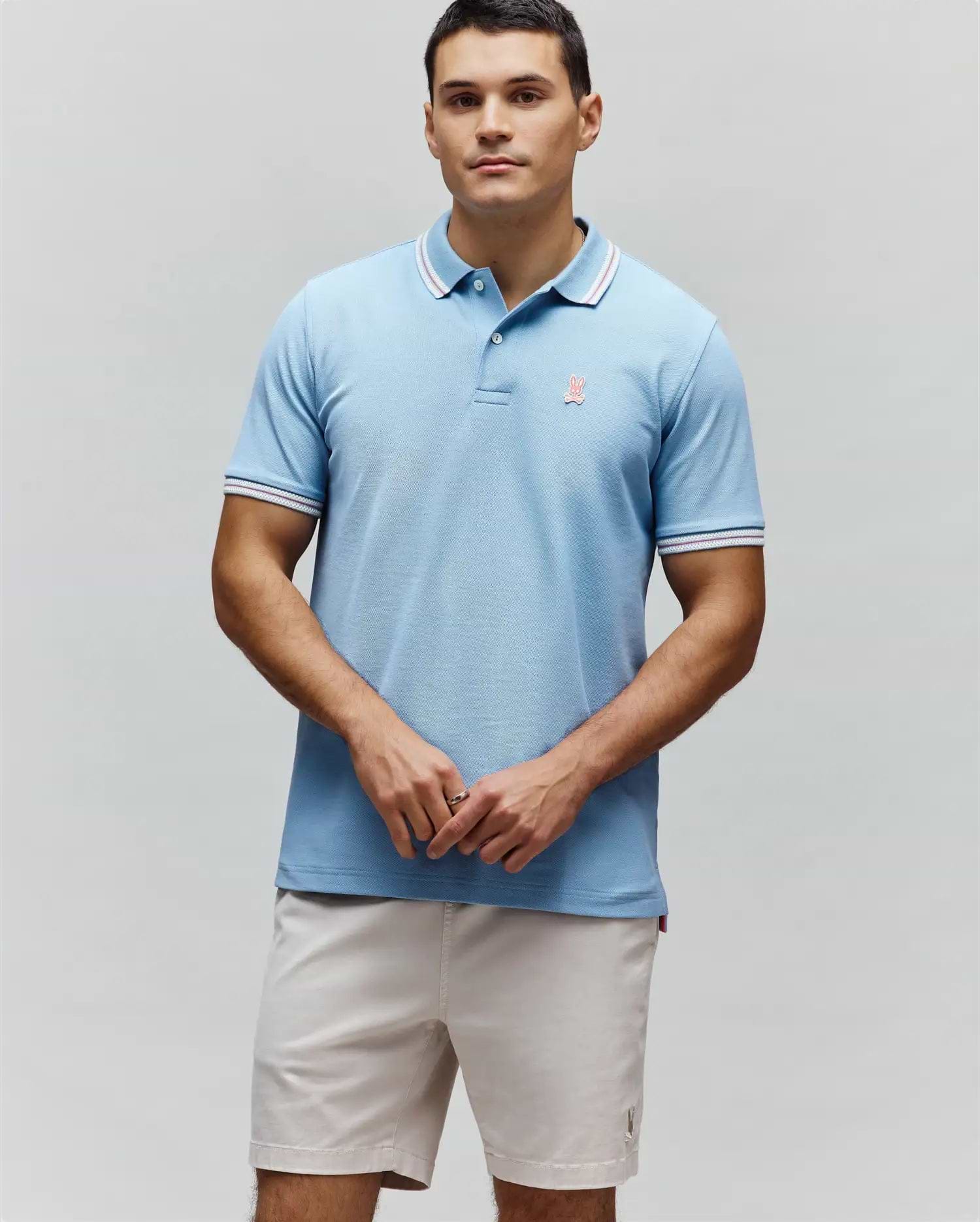Mens Clark Pique Polo, a light blue classic fit pique polo with white and red striped collar and cuffs, featuring a small embroidered pink Psycho Bunny logo on the left chest. (3)
