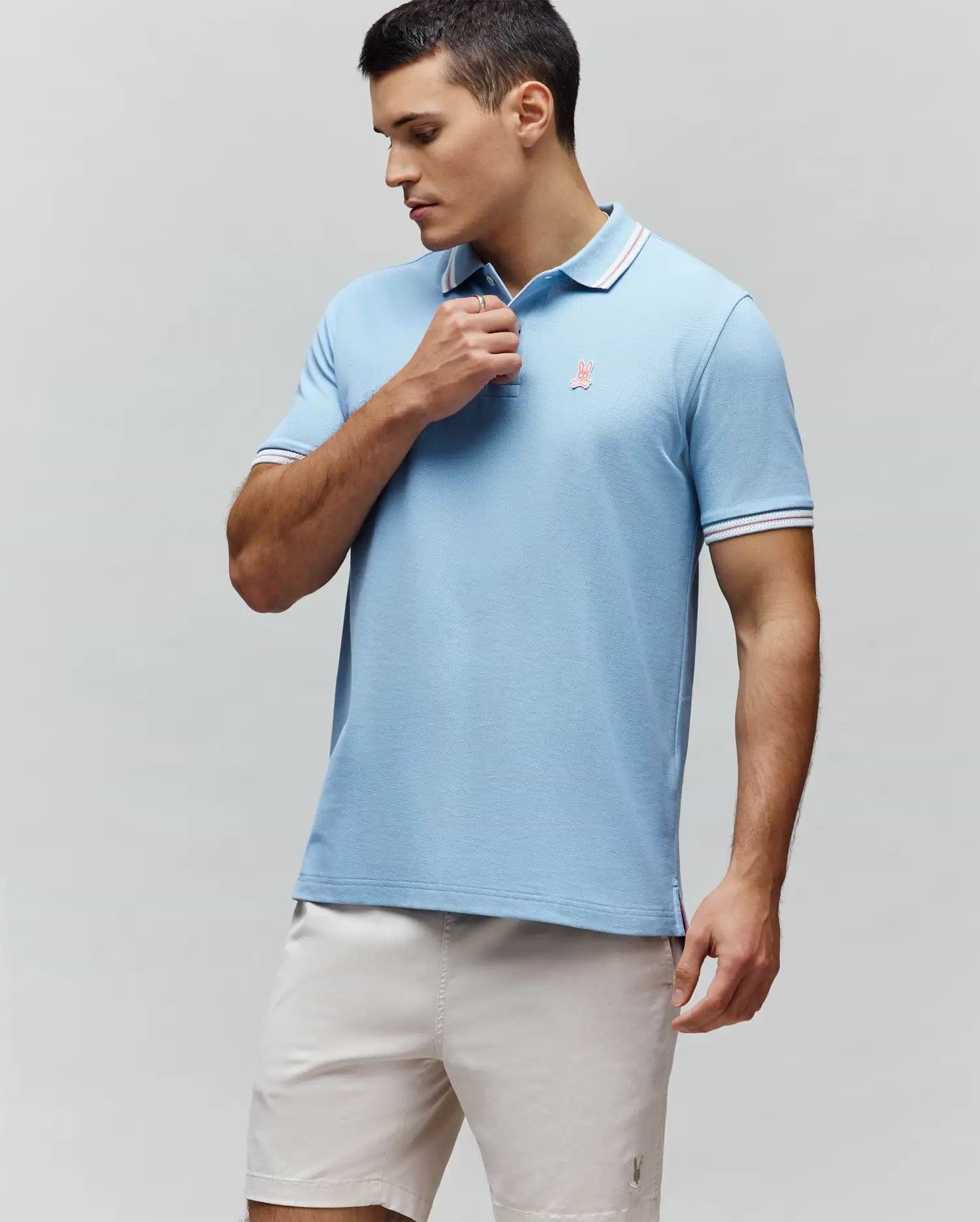 Mens Clark Pique Polo, sky blue classic fit pique knit with white and red striped collar and cuffs, featuring a small embroidered coral Psycho Bunny skull logo on the left chest and striped side vents. (1)