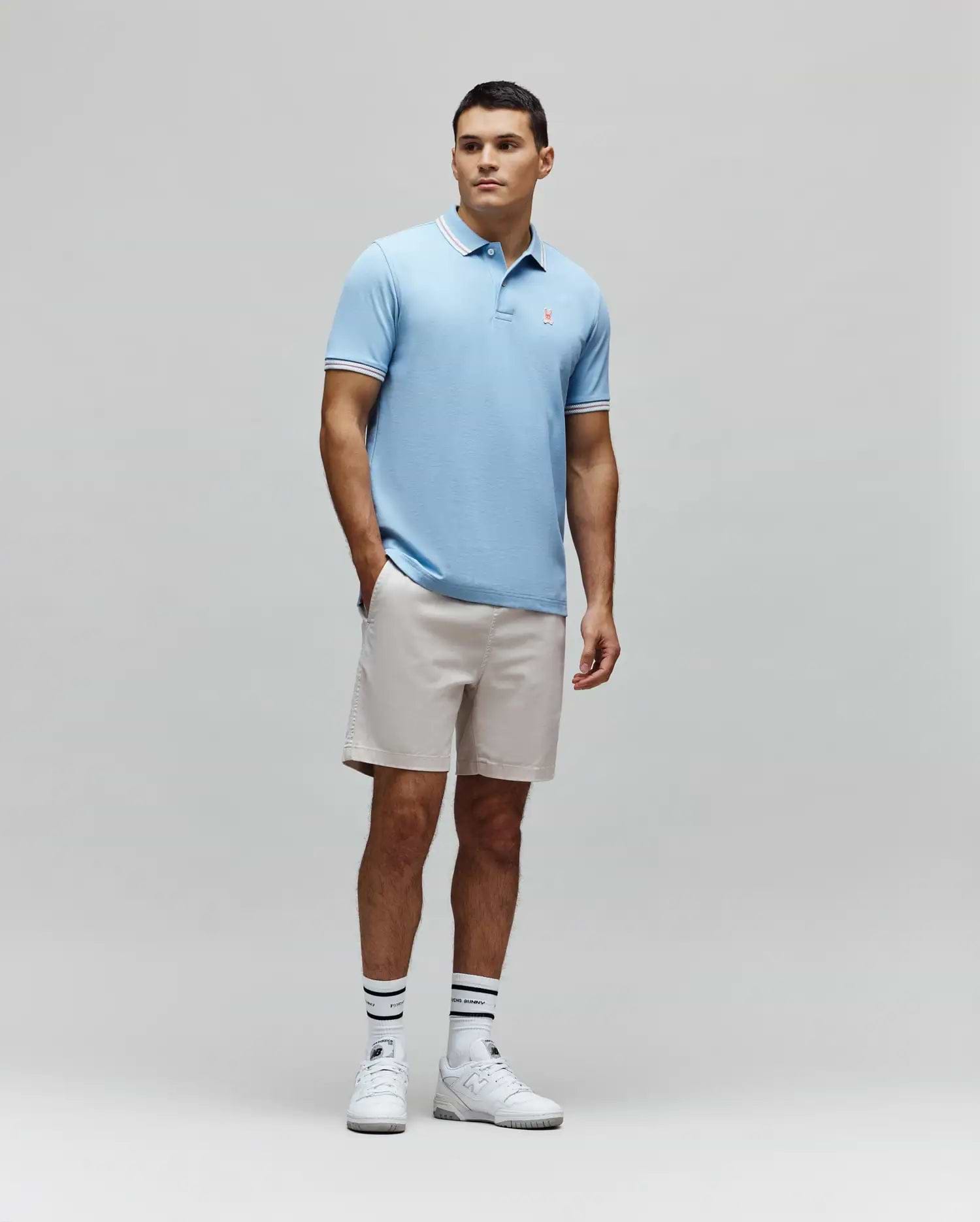 Mens Clark Pique Polo, a light blue classic fit pique polo with white and pink striped collar and cuffs, featuring a small embroidered pink Psycho Bunny skull logo on the left chest. (4)
