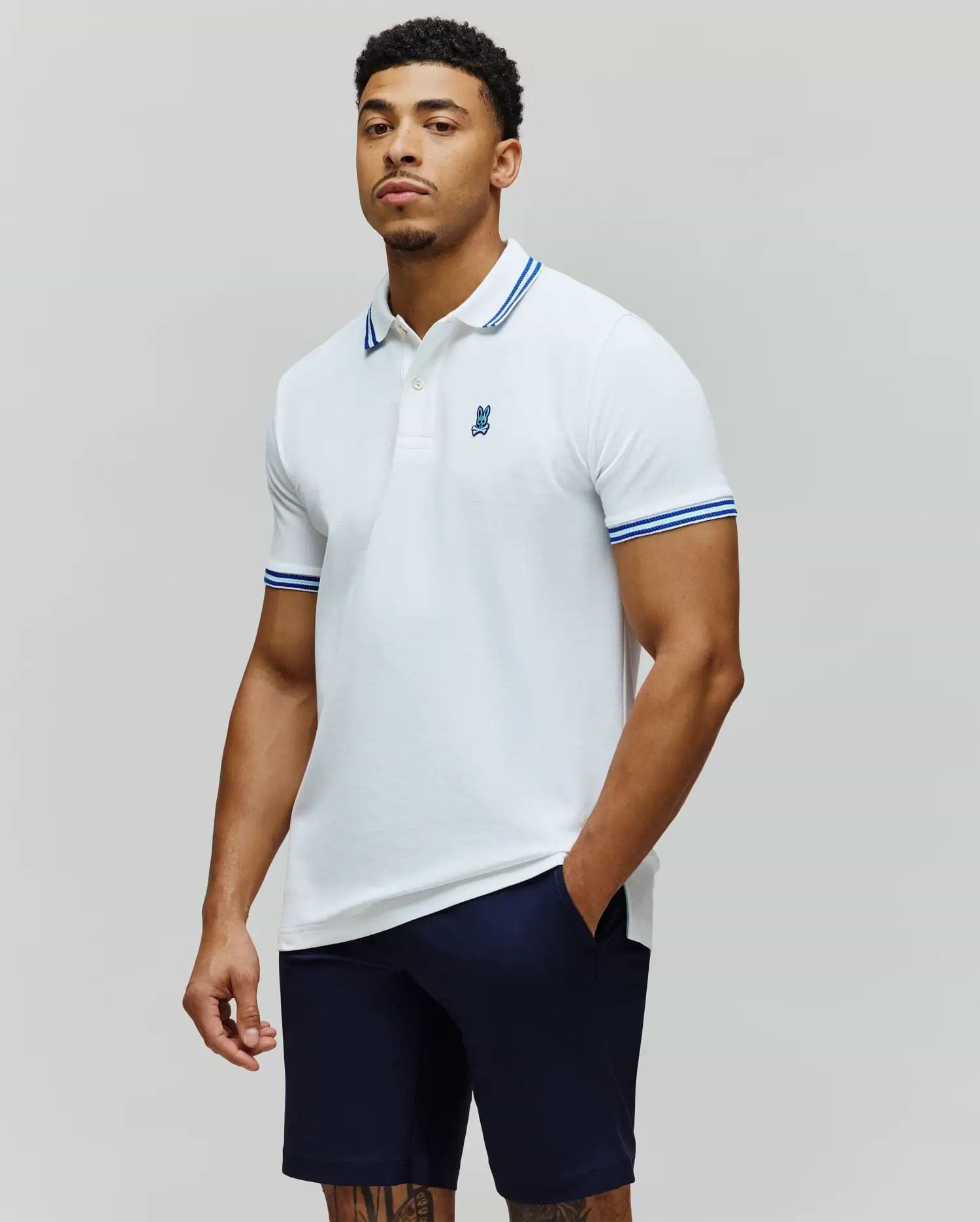 Mens Clark Pique Polo white classic fit pique polo with blue double-striped collar and cuffs, featuring a small embroidered blue Psycho Bunny skull logo on the left chest. (1)