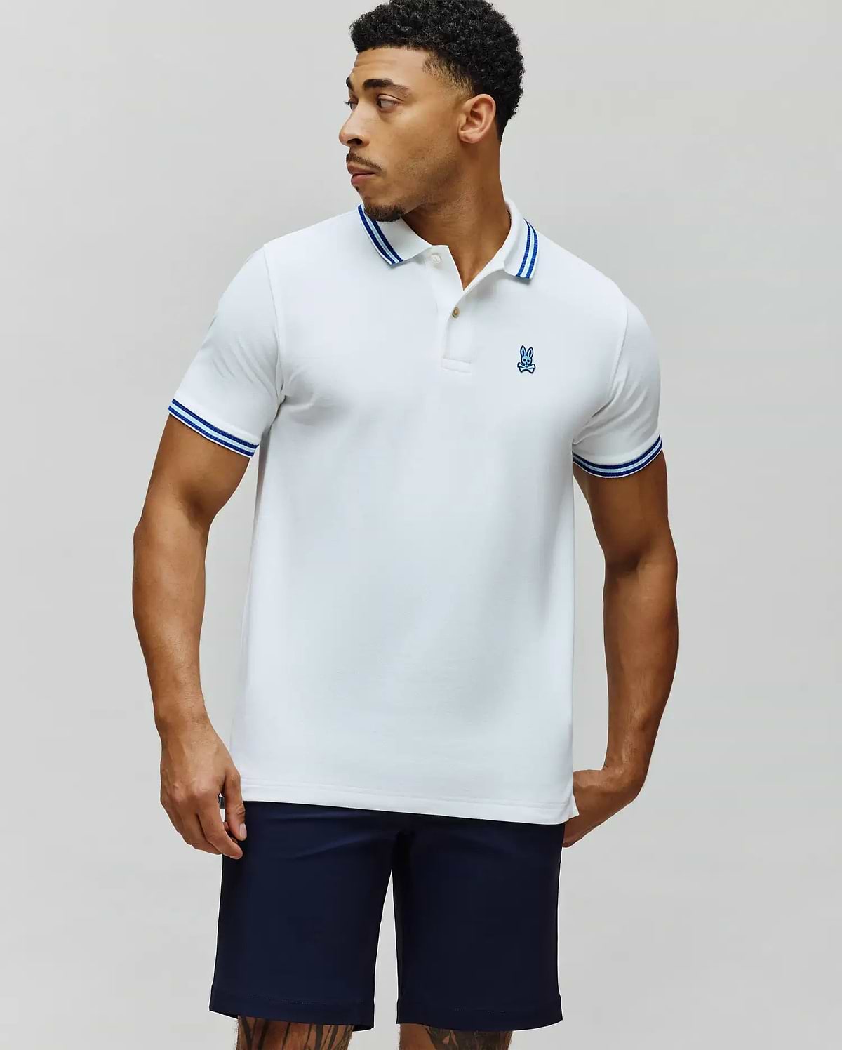 Mens Clark Pique Polo, a classic fit white pique polo with blue tipped collar and cuffs, featuring a small embroidered blue Psycho Bunny skull logo on the left chest. (3)
