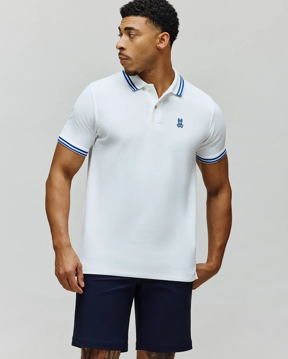 Mens Clark Pique Polo, a classic fit white pique polo with blue tipped collar and cuffs, featuring a small embroidered blue Psycho Bunny skull logo on the left chest. (3)