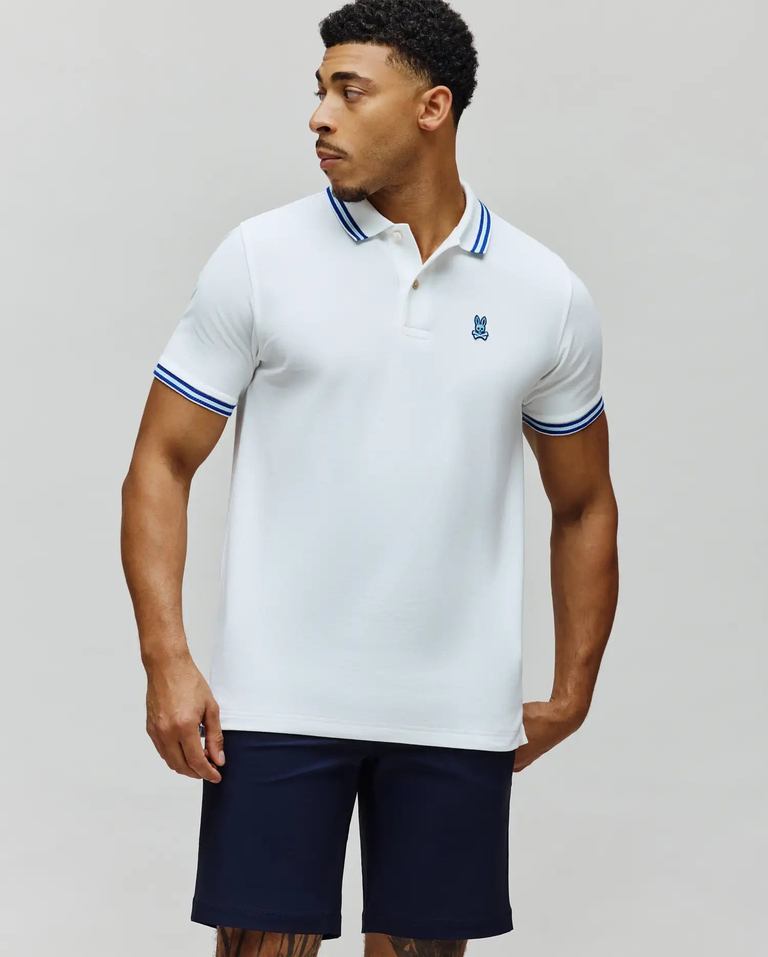 Mens Clark Pique Polo, a classic fit white pique polo with blue tipped collar and cuffs, featuring a small embroidered blue Psycho Bunny skull logo on the left chest. (3)