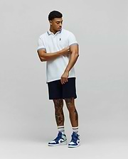 Mens Clark Pique Polo, a classic fit white pique polo shirt with blue double stripe accents on the collar and cuffs, featuring a small embroidered blue Psycho Bunny skull logo on the left chest. (4)