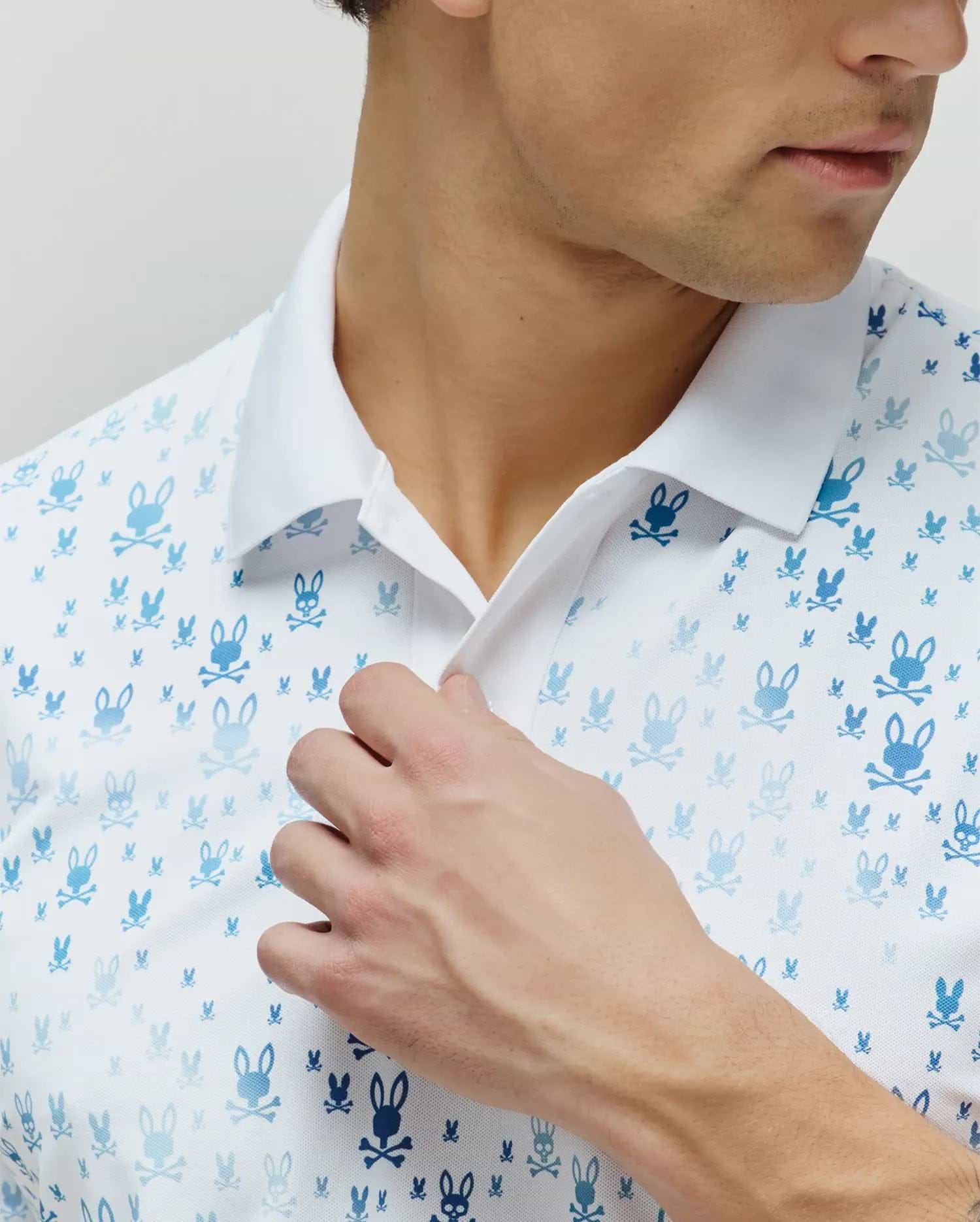 Mens Nev Sport Polo, white pique knit polo featuring an all-over gradient blue Psycho Bunny skull logo pattern in varying sizes, with a crisp white collar.