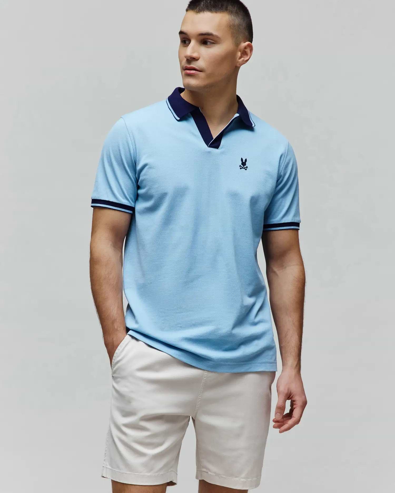 Mens Christiano Pique Polo in sky blue, featuring a classic fit, pique texture, navy V-neck collar, ribbed cuffs with navy and white stripes, and a small embroidered navy Psycho Bunny skull logo on the left chest. (1)