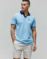 Mens Christiano Pique Polo in sky blue, featuring a classic fit, pique texture, navy V-neck collar, ribbed cuffs with navy and white stripes, and a small embroidered navy Psycho Bunny skull logo on the left chest. (1)