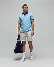 Mens Christiano Pique Polo in light blue, classic fit, with navy collar and cuffs, featuring an embroidered Psycho Bunny logo. Paired with beige shorts, white logo socks, and a navy Psycho Bunny tote bag. (3)