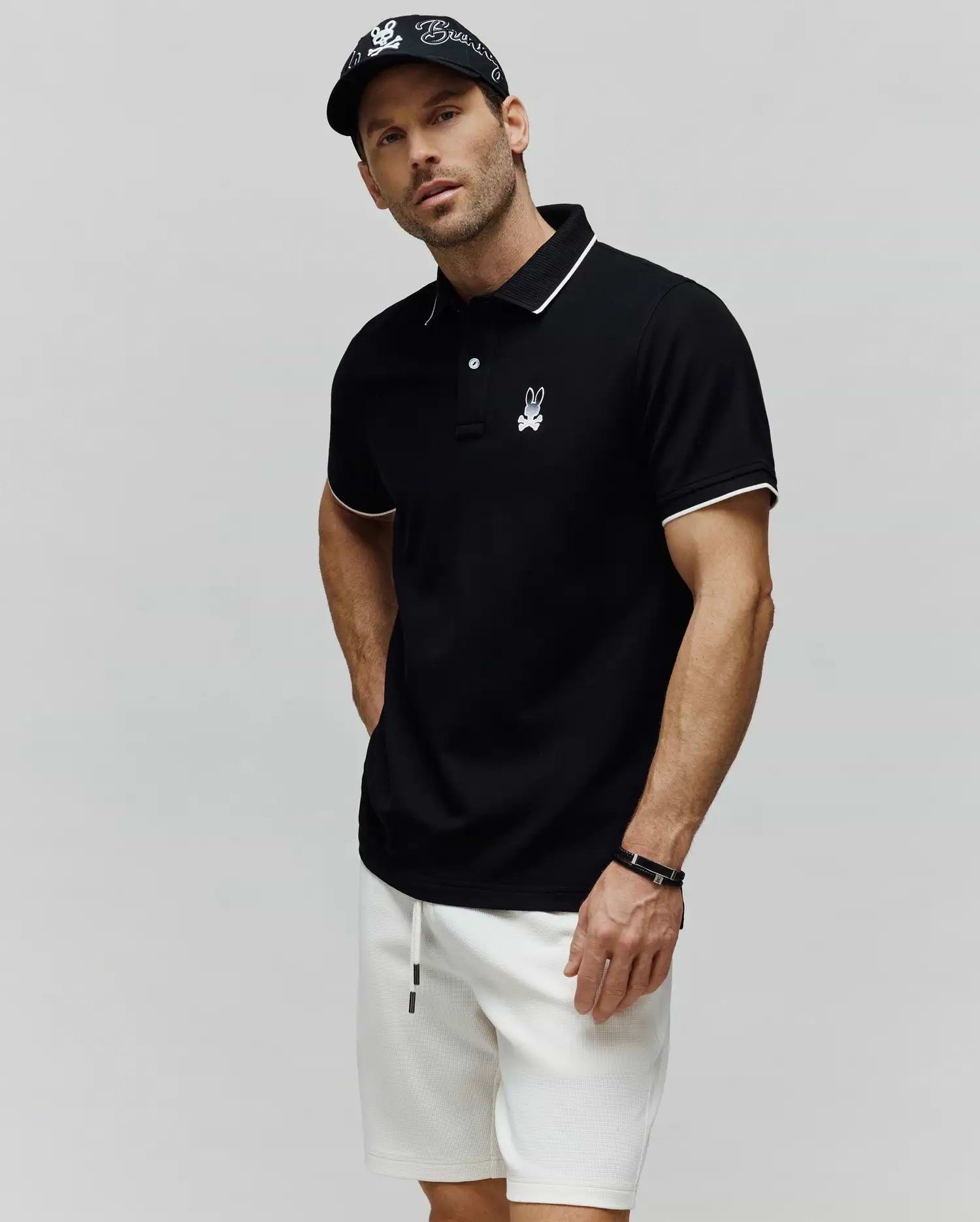 Black Mens Aram Pique Polo with white tipping on the collar and cuffs, featuring a two-button placket and an embroidered white Psycho Bunny skull logo on the left chest. (3)