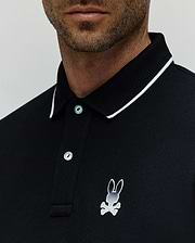 Black Mens Aram Pique Polo with a classic fit, featuring a white-tipped ribbed collar, two light blue buttons, and a medium embroidered white and grey Psycho Bunny skull logo on the left chest. (2)