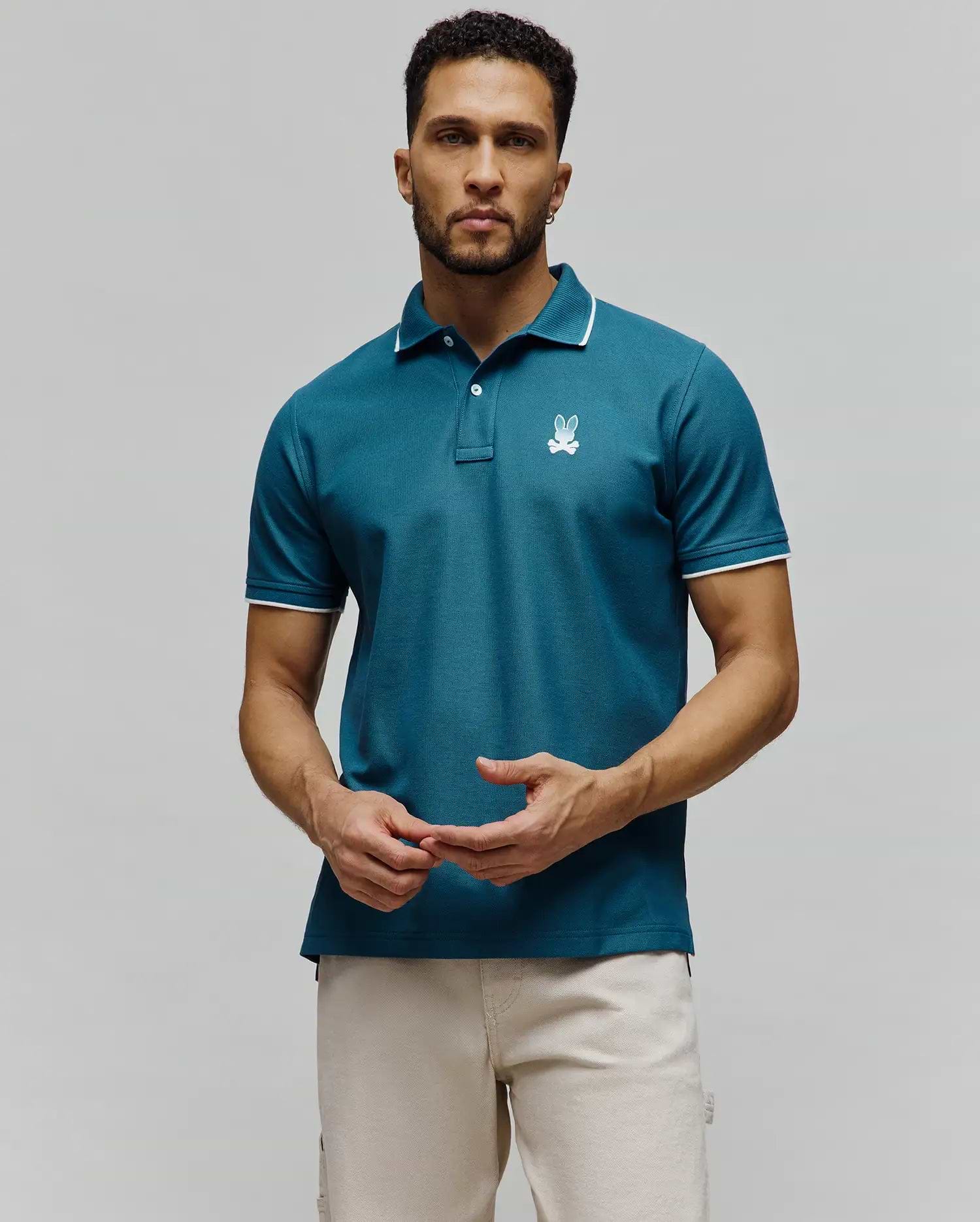 Mens Aram Pique Polo, a teal pique knit polo with white tipping on the collar and cuffs, featuring an embroidered white Psycho Bunny skull logo on the left chest in a classic fit. (4)