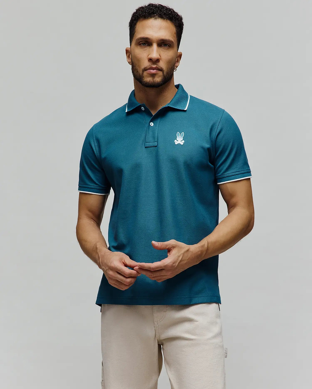 Mens Aram Pique Polo, a teal pique knit polo with white tipping on the collar and cuffs, featuring an embroidered white Psycho Bunny skull logo on the left chest in a classic fit. (4)