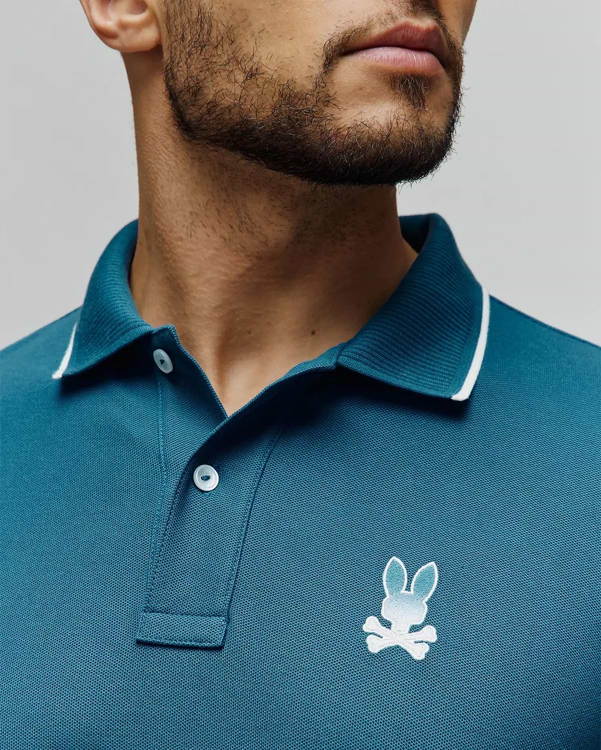 Mens Aram Pique Polo in teal, classic fit, pique knit, with a ribbed collar featuring white tipping, two white buttons, and a small embroidered white to light blue gradient Psycho Bunny skull logo on the left chest. (3)