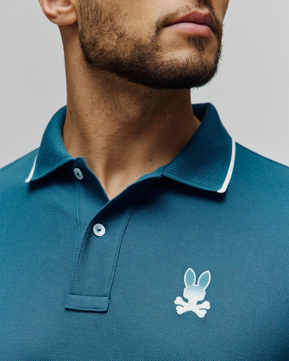 Mens Aram Pique Polo in teal, classic fit, pique knit, with a ribbed collar featuring white tipping, two white buttons, and a small embroidered white to light blue gradient Psycho Bunny skull logo on the left chest. (3)