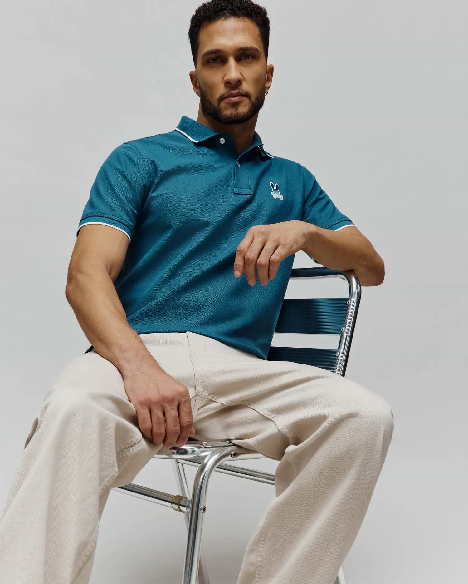 Mens Aram Pique Polo, a classic fit teal pique polo shirt with white tipping on the collar and sleeve cuffs, featuring a small embroidered Psycho Bunny skull logo on the left chest. (1)