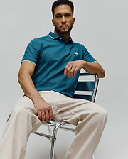 Mens Aram Pique Polo, a classic fit teal pique polo shirt with white tipping on the collar and sleeve cuffs, featuring a small embroidered Psycho Bunny skull logo on the left chest. (1)