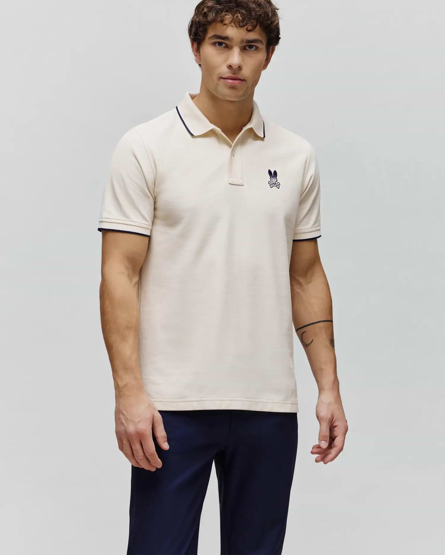 Mens Aram Pique Polo in cream, featuring a classic fit, textured pique fabric, navy blue tipping on the collar and sleeve cuffs, and a small embroidered Psycho Bunny skull logo on the left chest. (3)