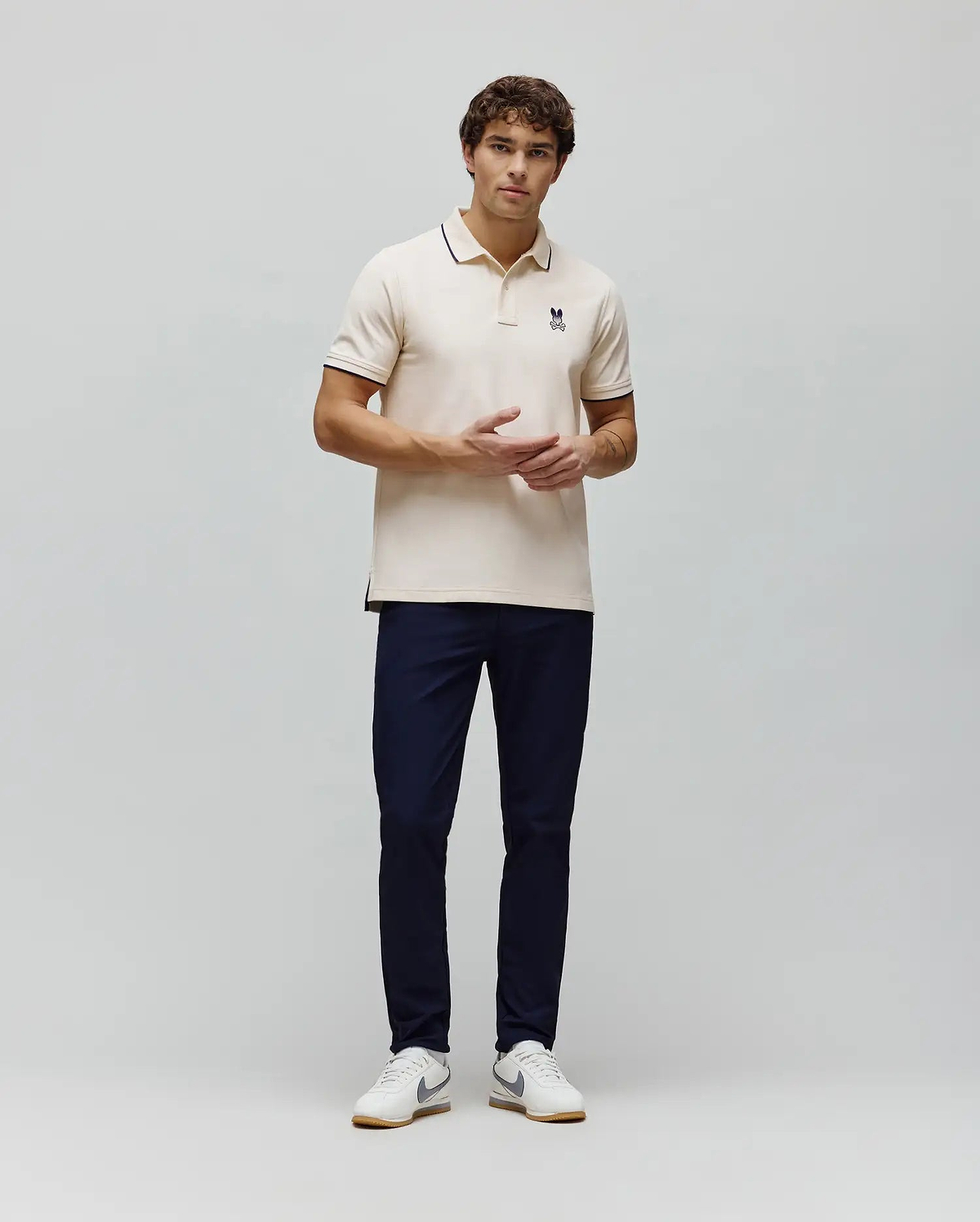 Mens Aram Pique Polo, a cream classic fit pique polo with navy blue tipped collar and cuffs, featuring a small embroidered navy blue Psycho Bunny skull logo on the left chest. (4)