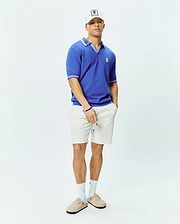 Mens Innis Polo, a vibrant blue classic fit textured knit polo with white tipped collar and cuffs, featuring a small embroidered Psycho Bunny skull logo on the left chest, and relaxed off-white textured drawstring shorts. (4)