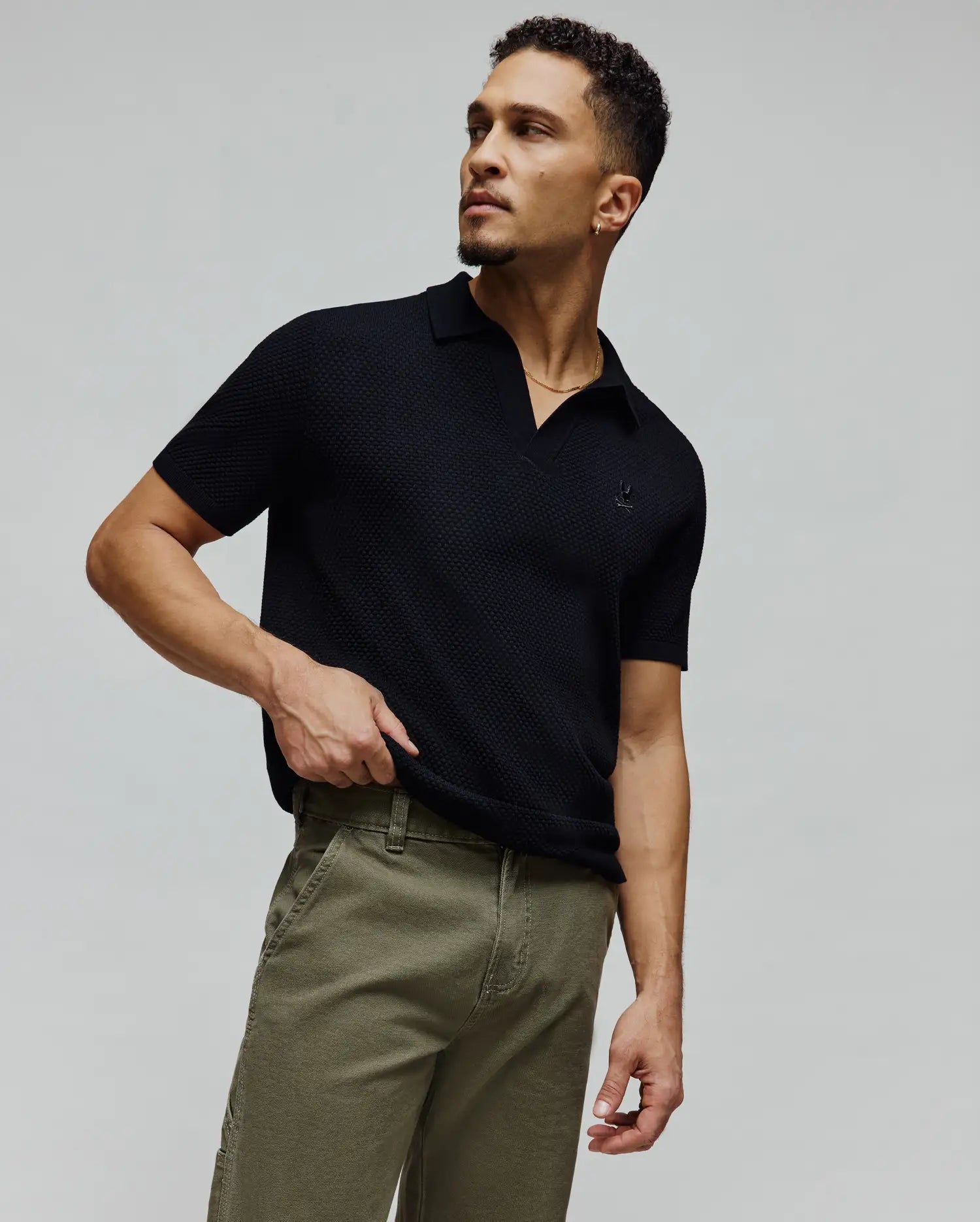 Mens Devon Knit Polo, a black textured knit short-sleeve polo with a classic fit, featuring a small embroidered Psycho Bunny skull logo on the left chest and an open collar.