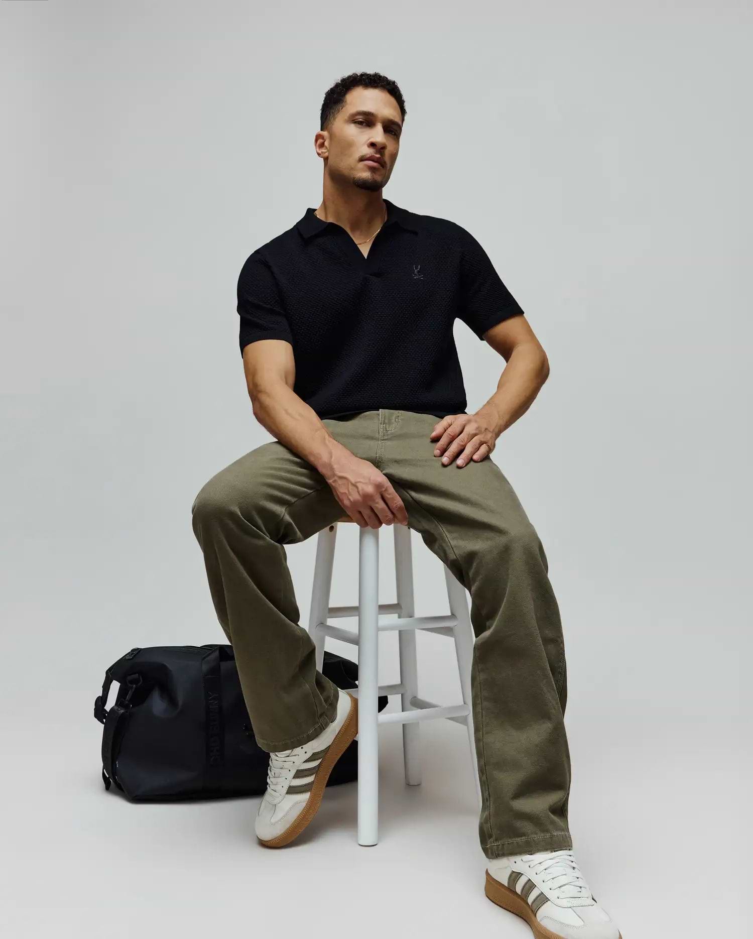 Mens Devon Knit Polo, a black textured knit polo shirt with an open collar and a small embroidered Psycho Bunny skull logo on the left chest, offering a classic fit.