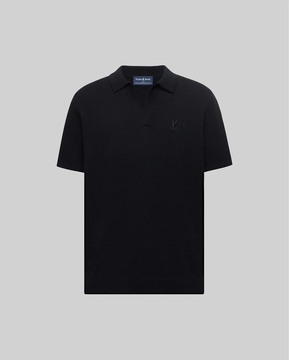 Mens Devon Knit Polo, a black classic fit polo in textured knit fabric with an open collar and a small, tonal black embroidered Psycho Bunny skull logo on the left chest.