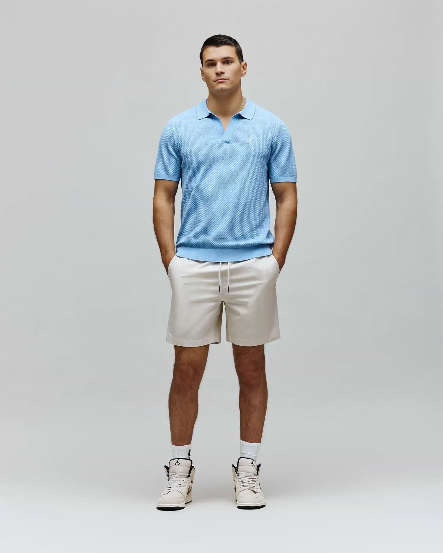 Mens Devon Knit Polo in light blue, featuring a textured knit fabric, open collar, and a small white embroidered Psycho Bunny skull logo on the left chest for a classic fit.