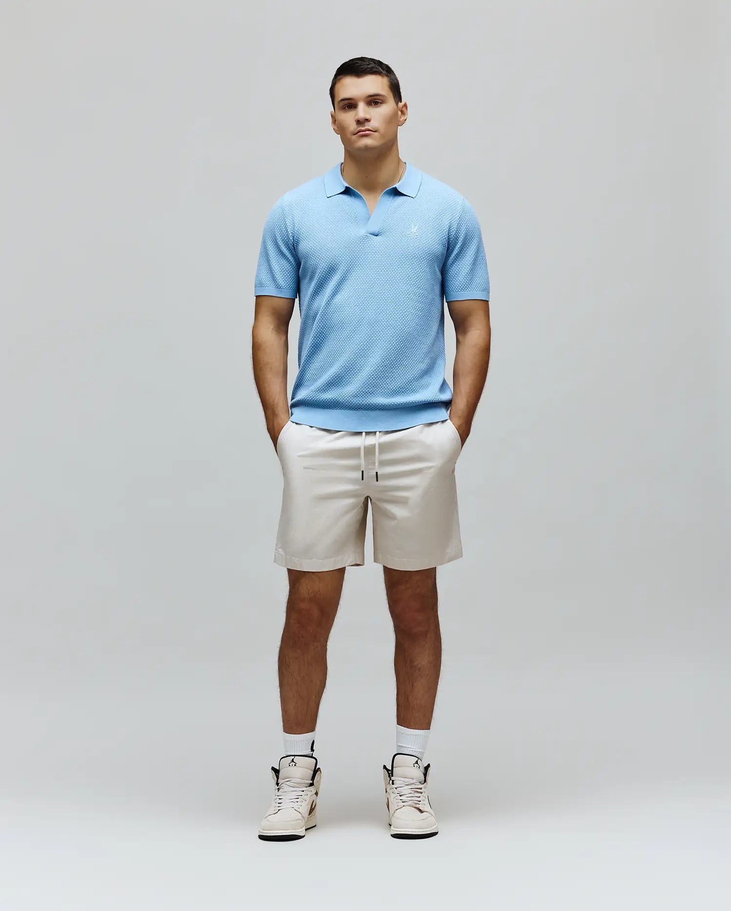 Mens Devon Knit Polo in light blue, featuring a textured knit fabric, open collar, and a small white embroidered Psycho Bunny skull logo on the left chest for a classic fit.
