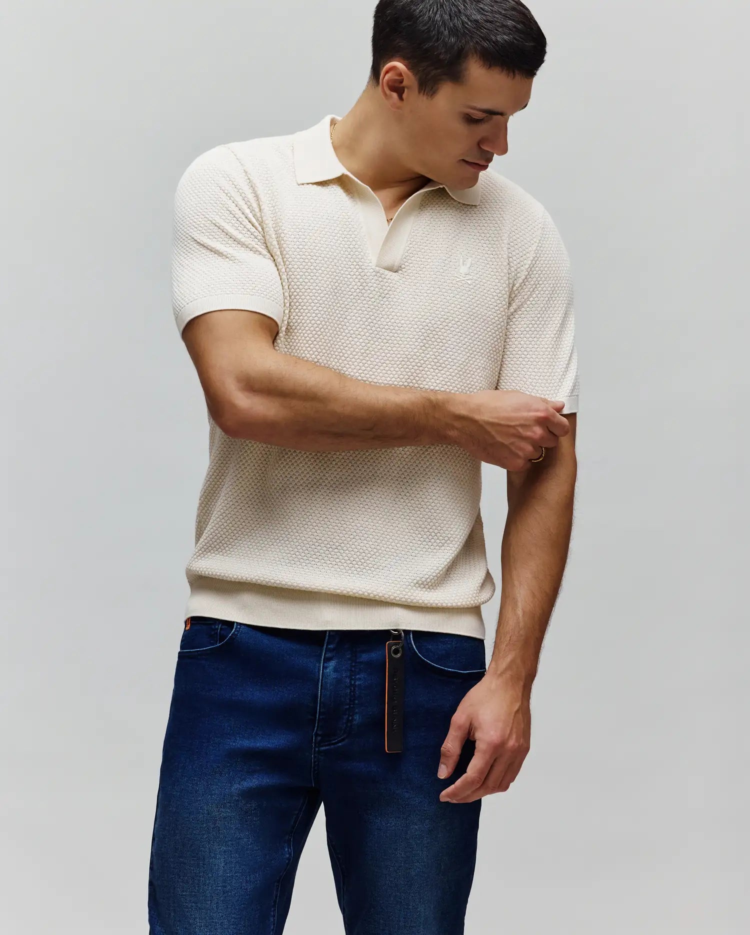Mens Devon Knit Polo in cream, featuring a textured knit fabric, classic fit, ribbed collar, two-button placket, and a small tonal embroidered Psycho Bunny skull logo on the left chest.