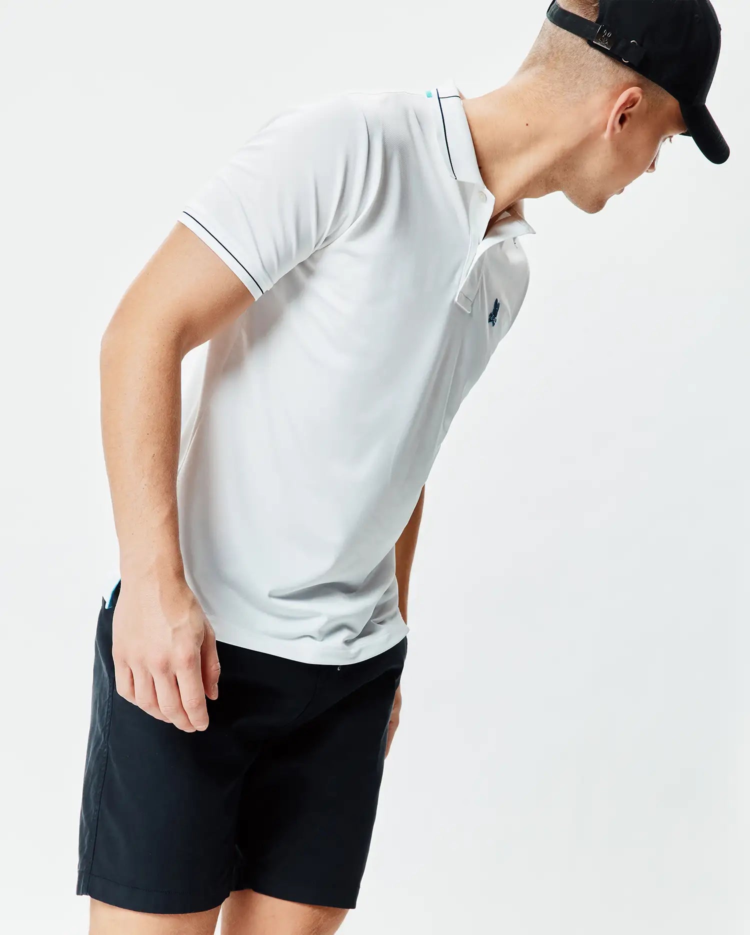 Mens Edwin Sport Polo, a white classic fit performance knit polo with black tipping on the collar and sleeves, a light blue inner collar stripe, and a small embroidered teal Psycho Bunny skull logo on the left chest.