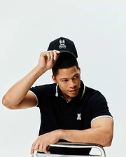 Black Mens Holden Pique Polo with light grey tipping on collar and cuffs, featuring a small embroidered Psycho Bunny logo on the left chest. Also a black cap with a large white embroidered Psycho Bunny logo.